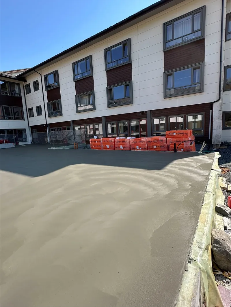 Ny betongflate under utjevning foran et leilighetsbygg