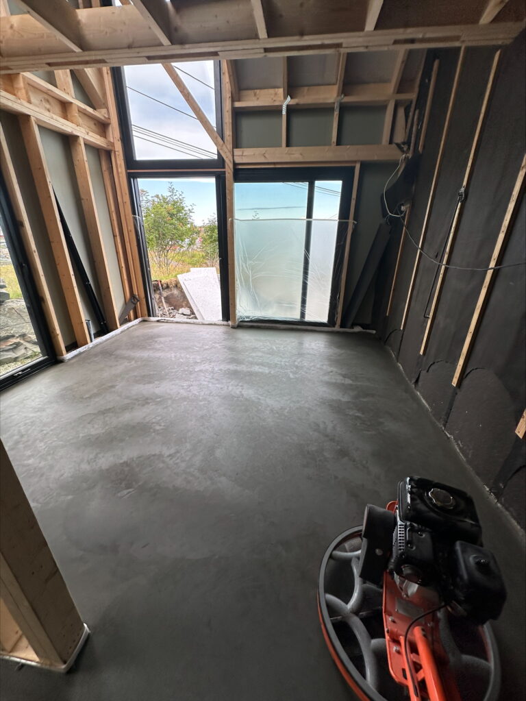 Nytt betonggulv under støping i et oppussingsprosjekt, med store vinduer og treverk rundt.