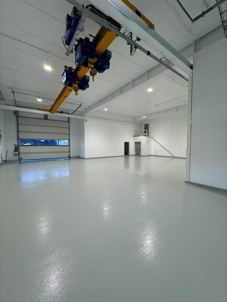 Gulvstøp og avretting i stort industrilokale med høydekran og hvite vegger.